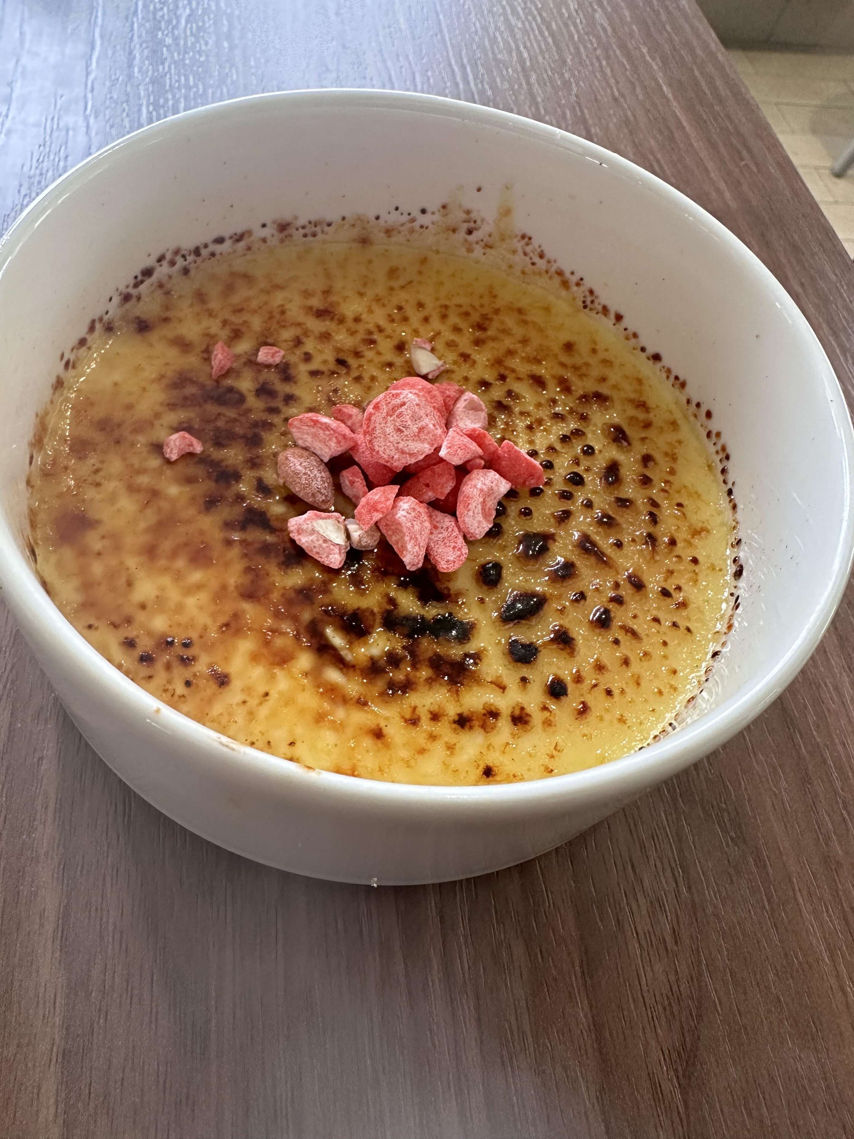 A bowl of food with a creamy texture and a browned top, placed on a wooden surface.