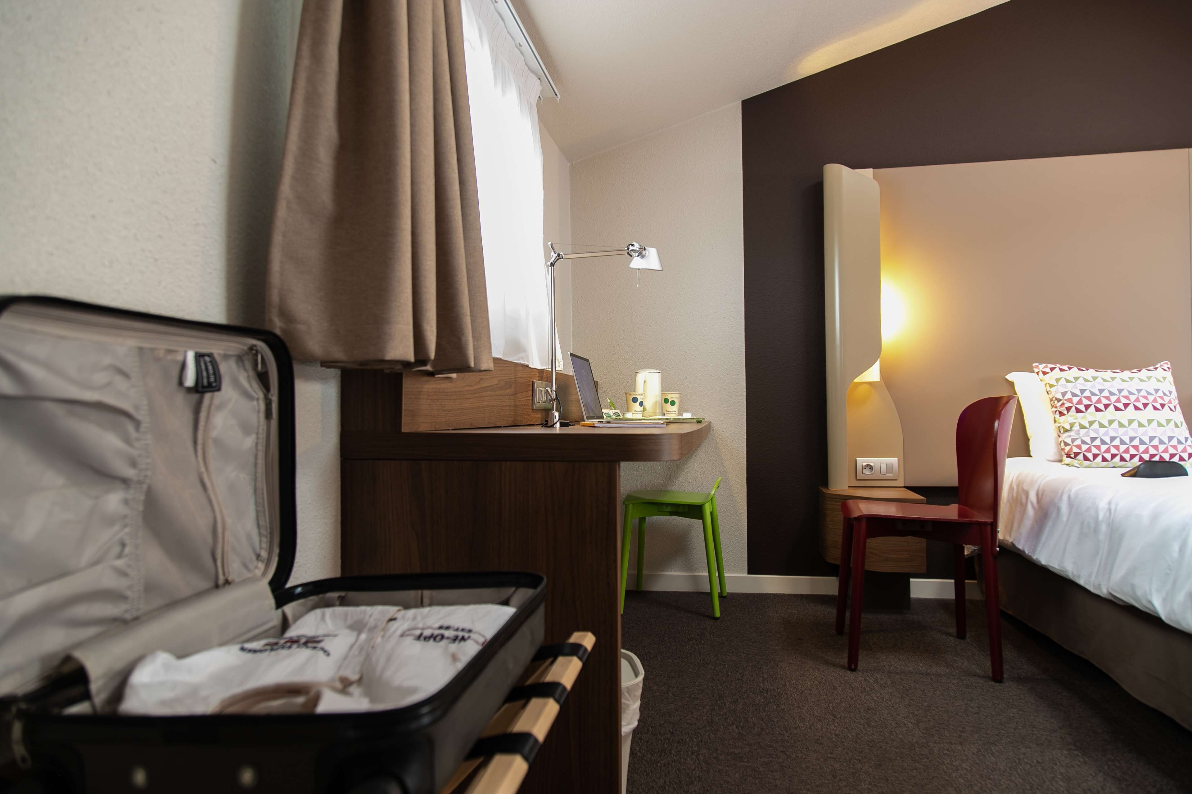 Une chambre d’hôtel avec un lit, un bureau, une chaise, une lampe et une valise.