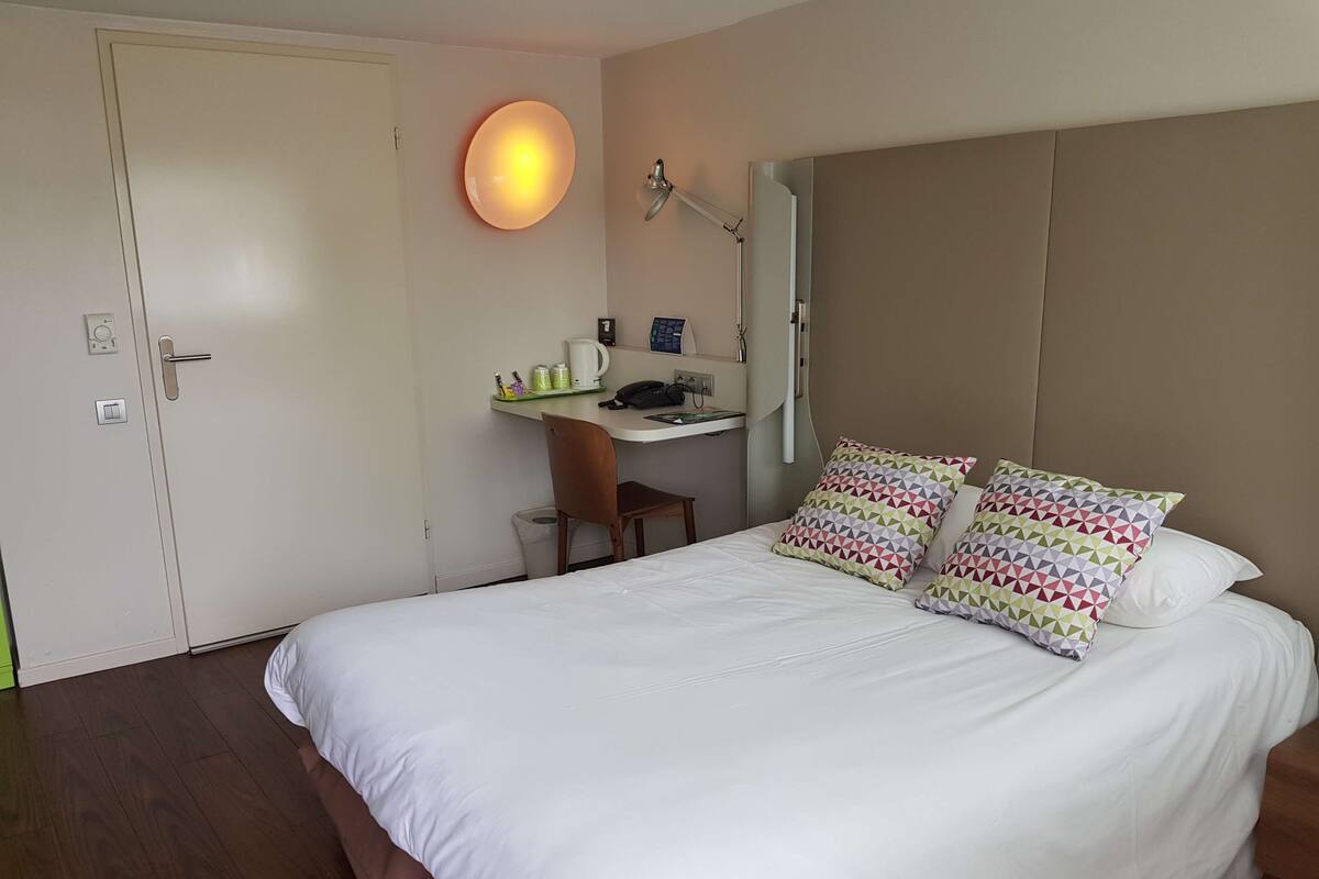 A neatly arranged hotel room with a bed, a desk, and a chair.