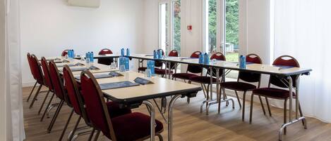 A conference room with multiple tables and chairs, large windows, and an air conditioning unit.