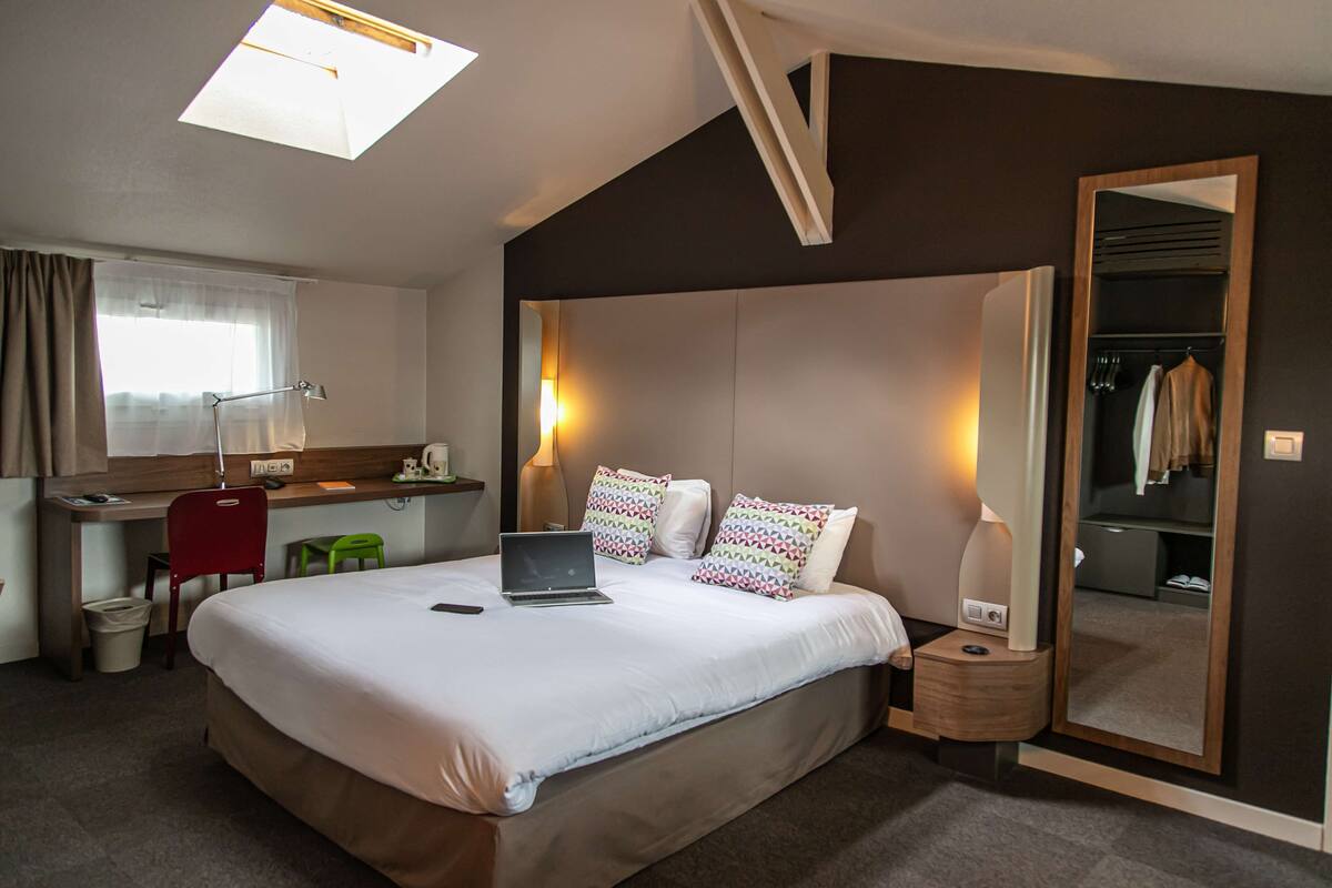A hotel room with a bed, desk, chair, and a mirror.