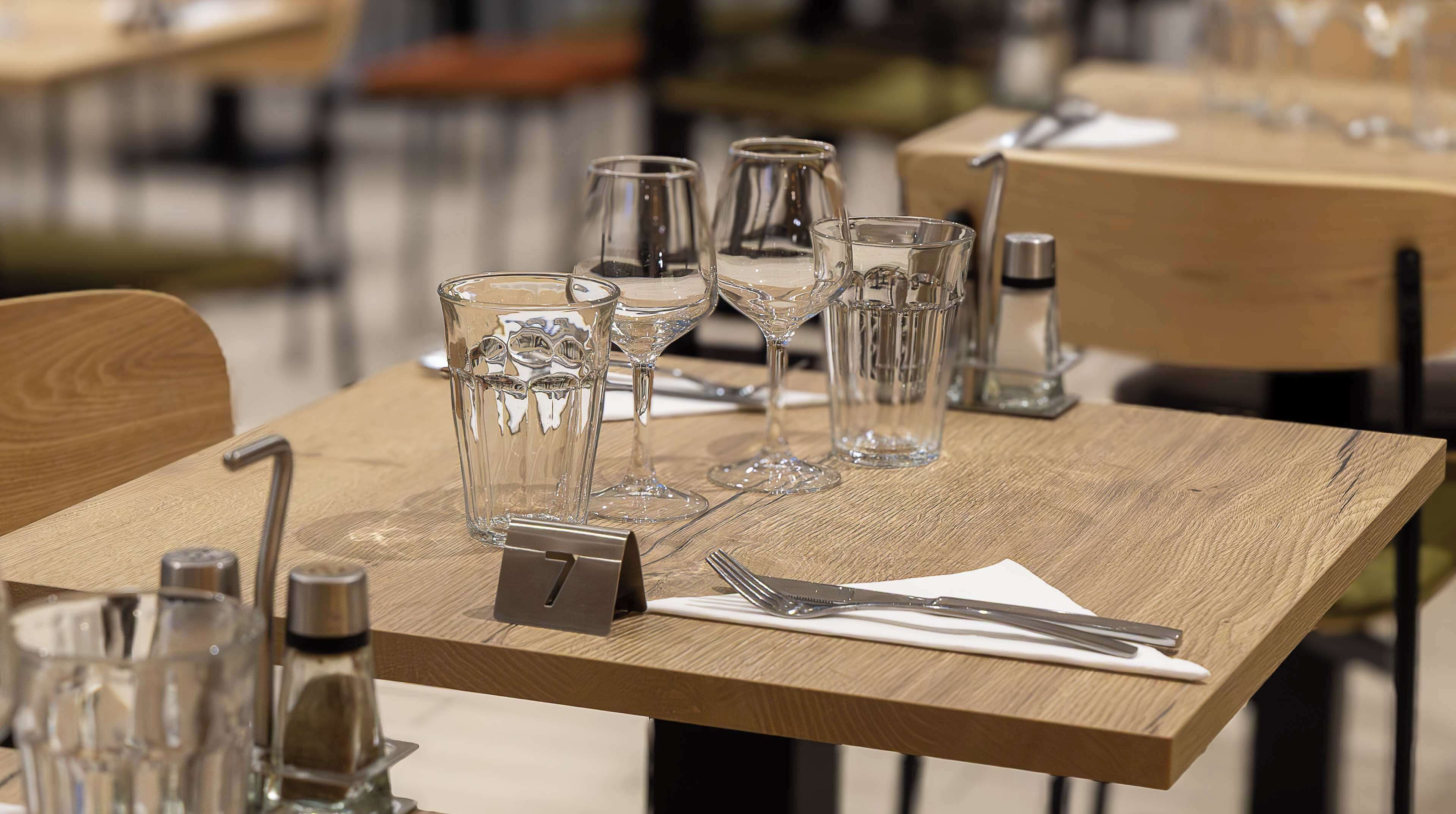 A dining table with clear glassware, a menu holder, and cutlery.