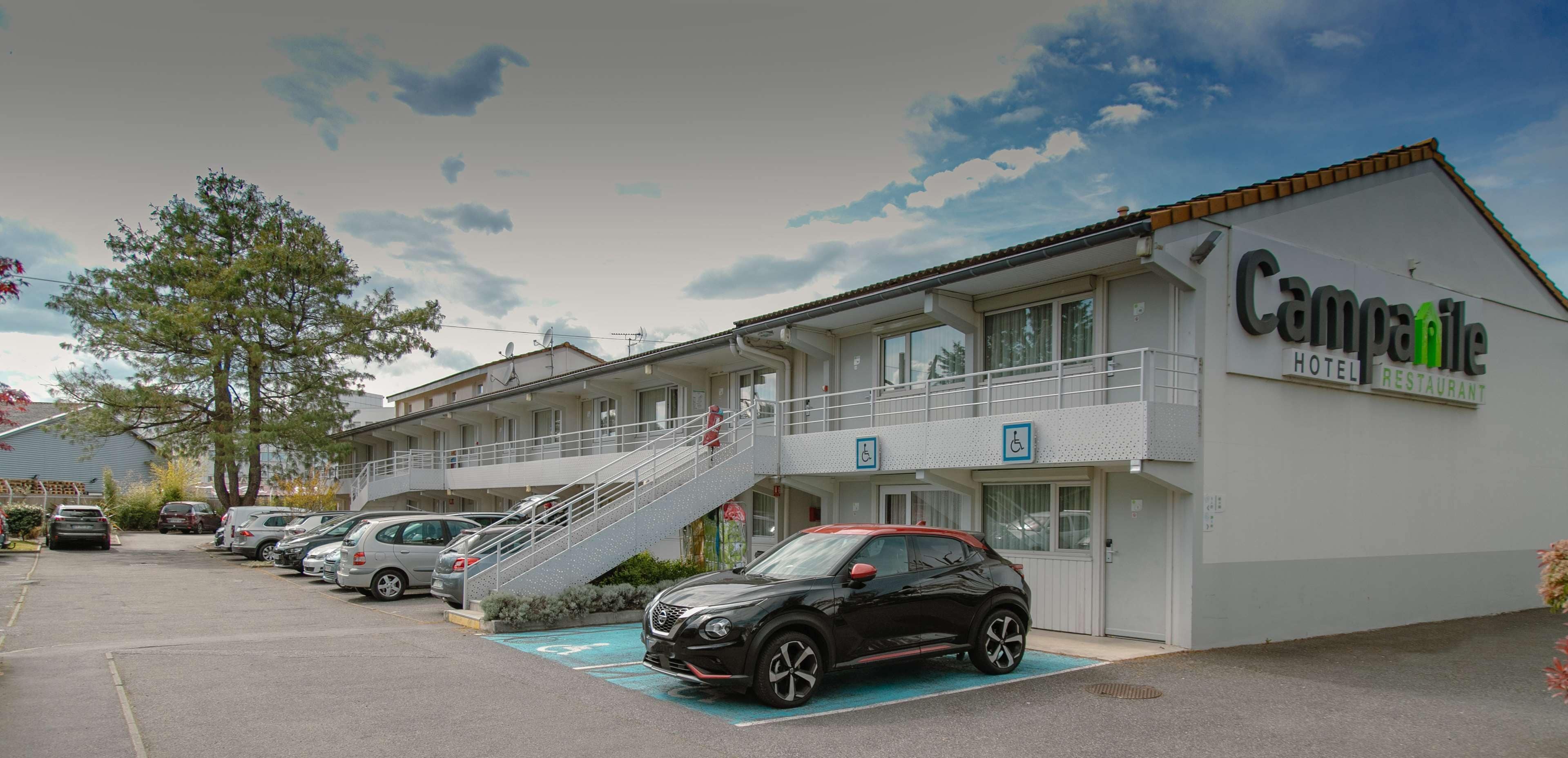 Un hotel con estacionamiento, una escalera que conduce a la entrada y un letrero que indica acceso para sillas de ruedas.
