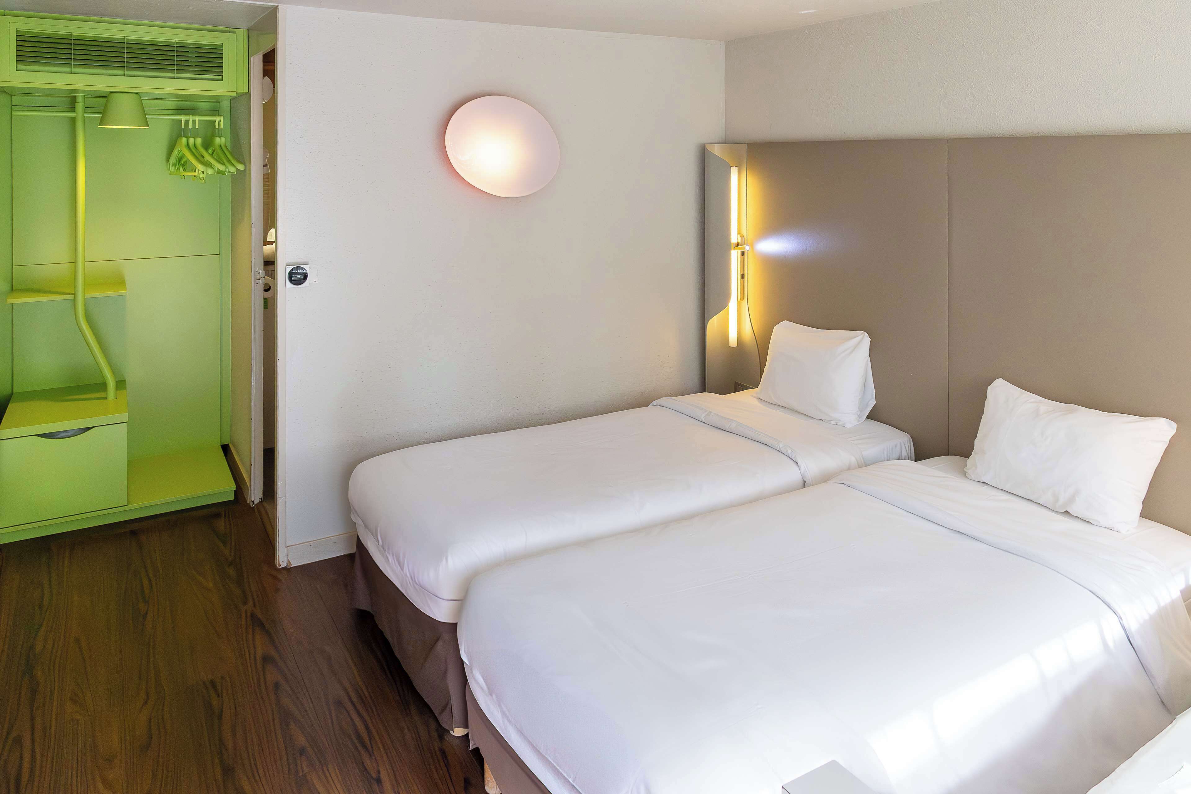 Habitación de hotel con dos camas, un armario verde, una lámpara de pared y un espejo.