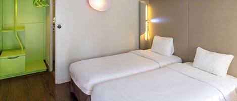 Habitación de hotel con dos camas, un armario verde, una lámpara de pared y un espejo.