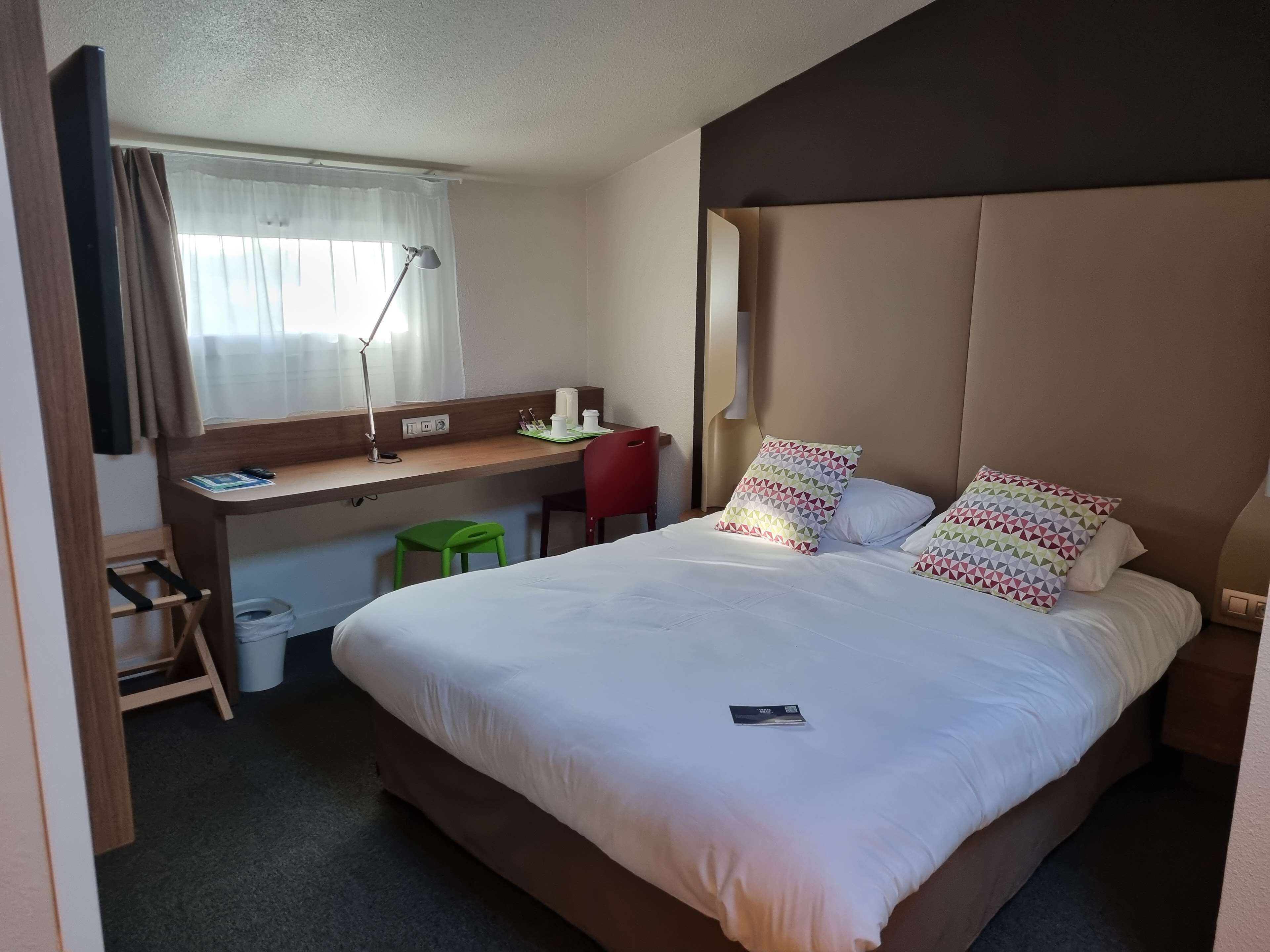 A hotel room with a bed, a desk, a chair, and a window with curtains.