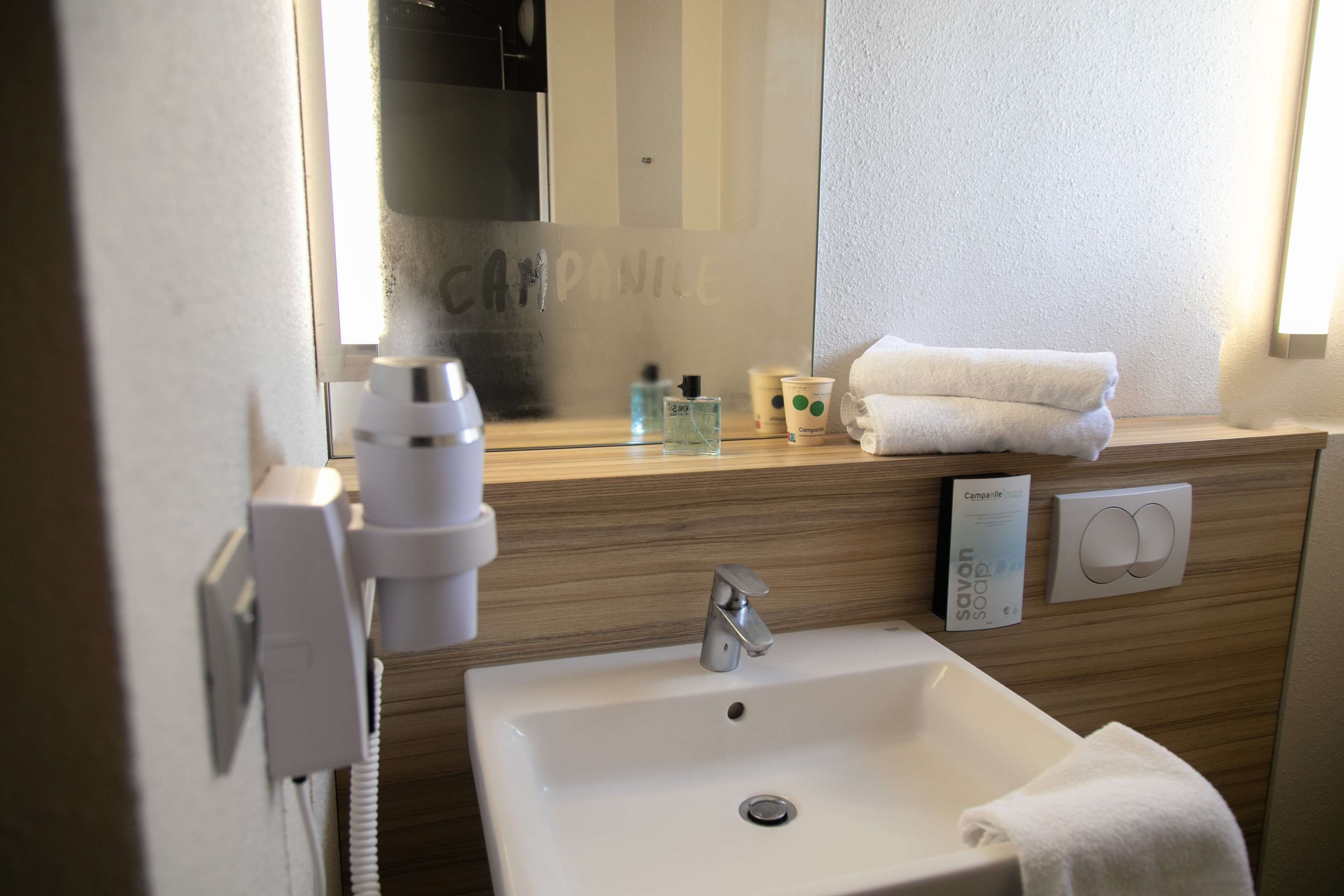 Ein Badezimmer mit einem weißen Waschbecken, einem Spiegel, einem Handtuch und einer Seifenspender.