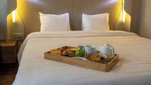A neatly made bed with white linens, a tray of breakfast items including toast, fruit, and a mug, and a bedside table with a lamp. - Hotel Campanile Toulouse - Blagnac Aéroport (Blagnac)