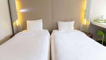 A hotel room with two single beds, a bedside table with a lamp, and a small desk with a chair.