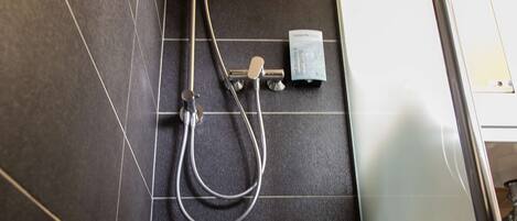 A shower area with a handheld showerhead, a wall-mounted faucet, and a control panel.