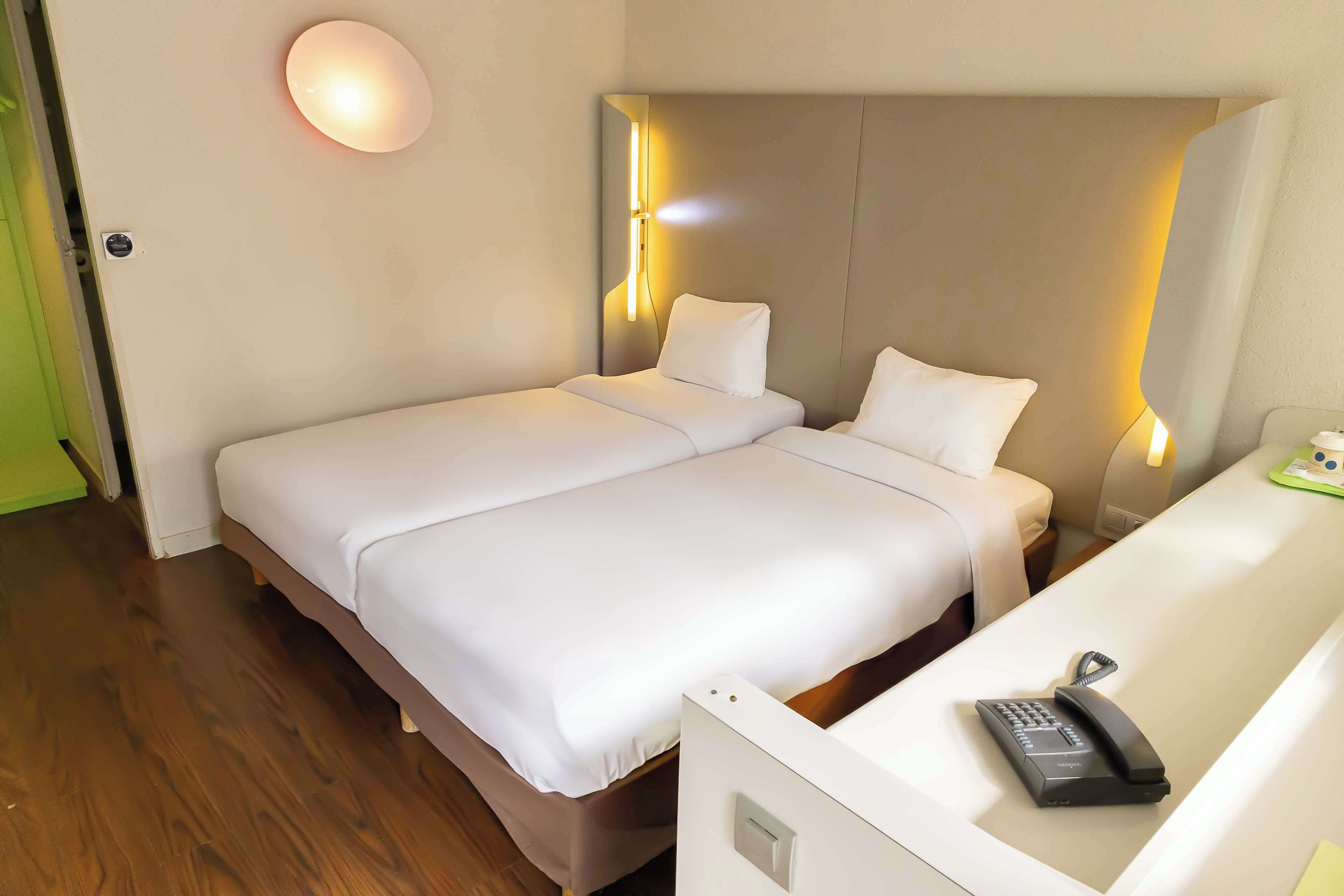 A hotel room with a double bed, bedside lamps, a desk with a telephone, and a green door.