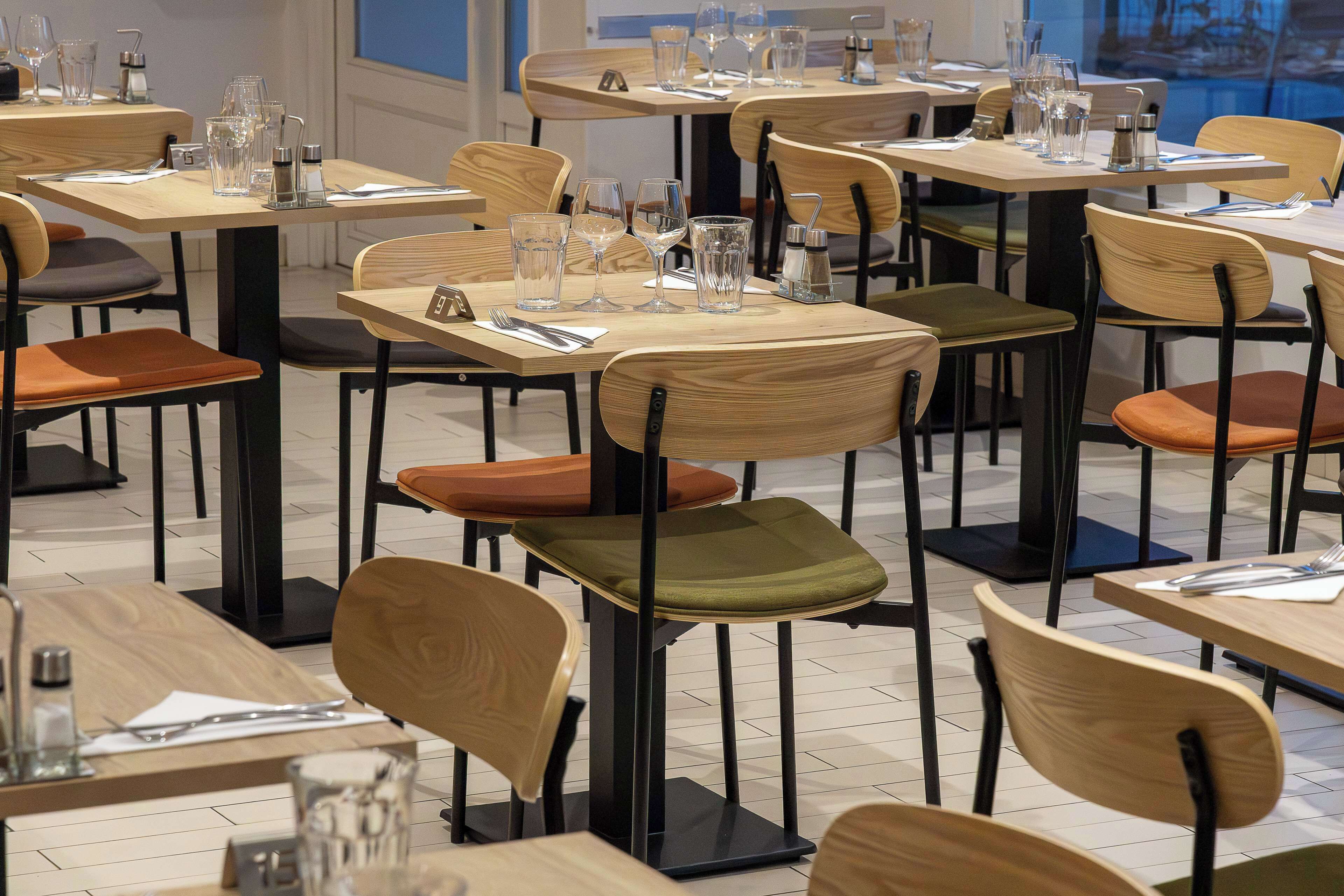 A restaurant with multiple tables and chairs, each set with cutlery and glasses.