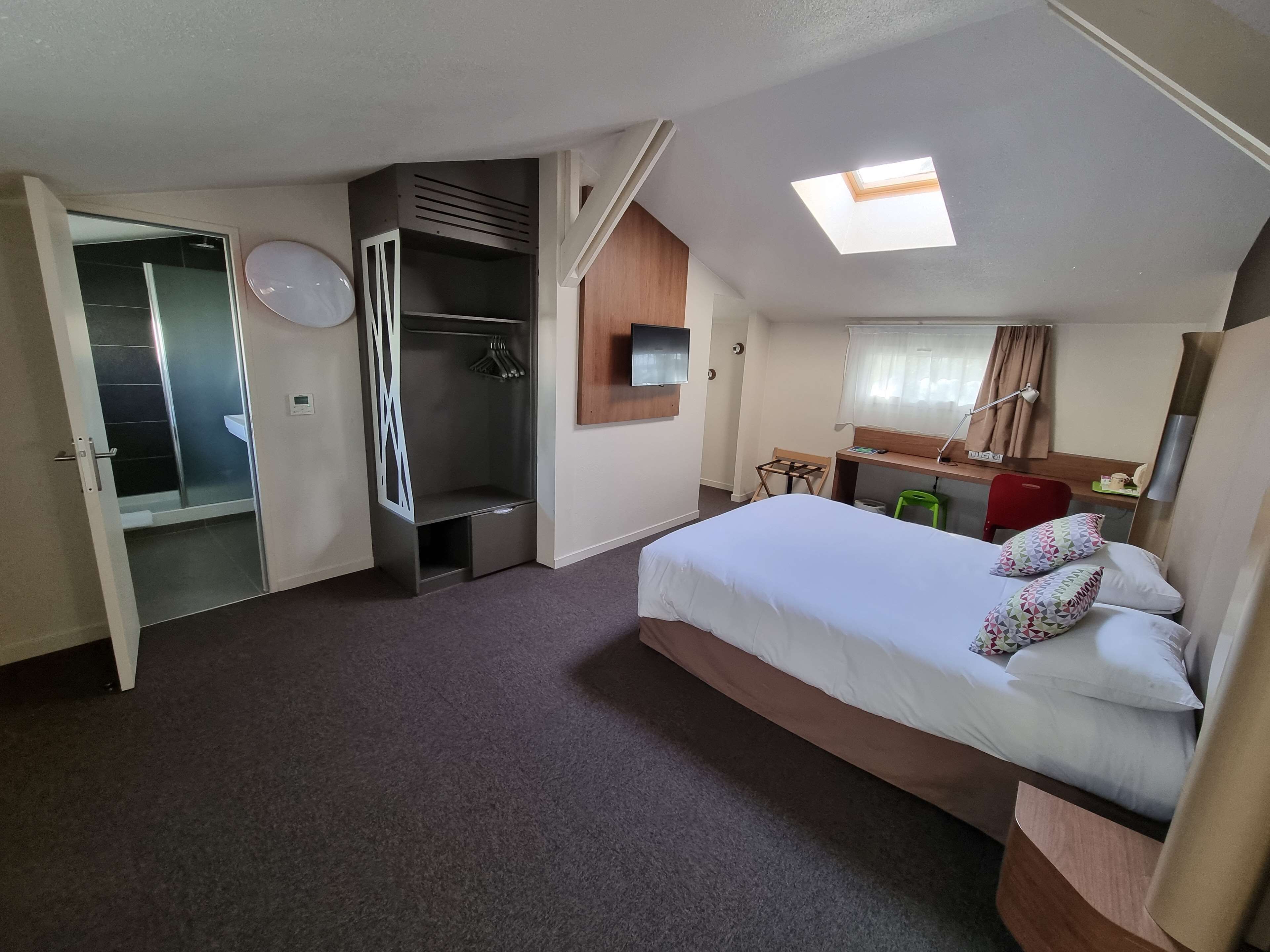 Quarto de hotel com cama, guarda-roupa, secretária, cadeira, mesinha e zona de duche.