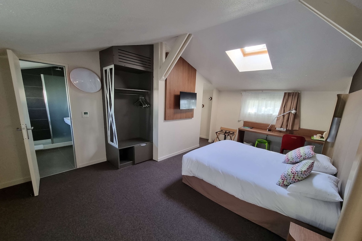 Quarto de hotel com cama, guarda-roupa, secretária, cadeira, mesinha e zona de duche.