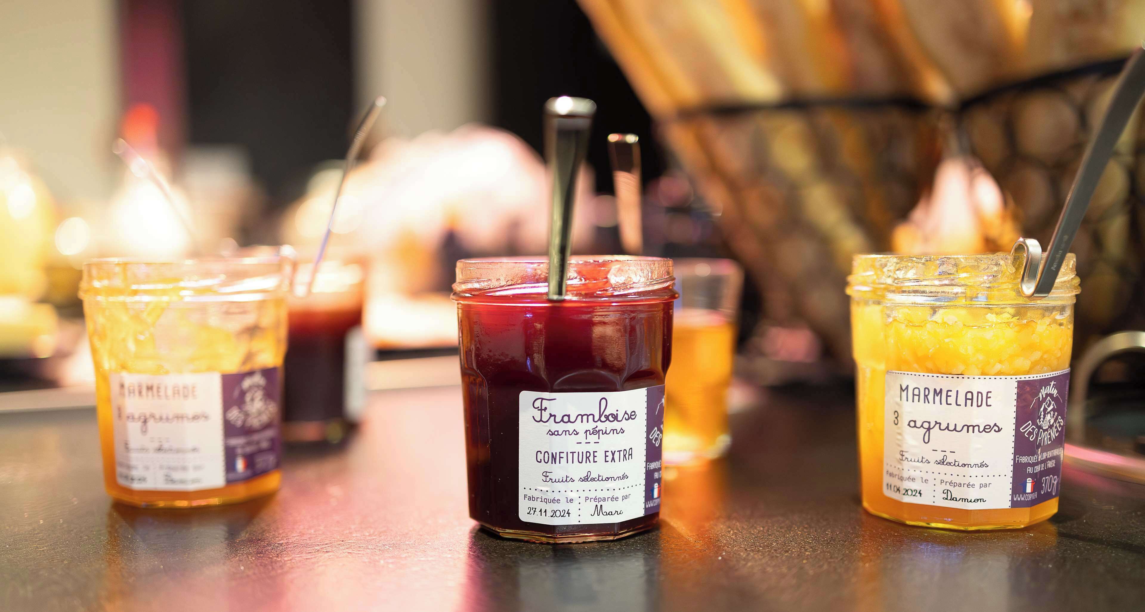 Three jars of Marmalade on a table with candles in the background.