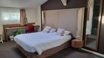Una habitación de hotel con una cama grande, un escritorio, una silla, un espejo y un tragaluz.
