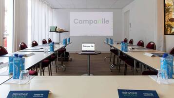 A conference room with a presentation screen displaying 'Campanile', a laptop on a central table, and water bottles on each table.