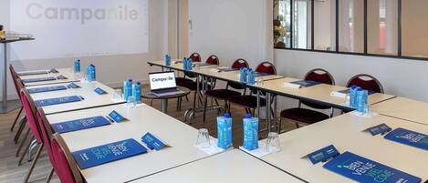 Un salón de conferencias con mesas, sillas y una pantalla para presentaciones.