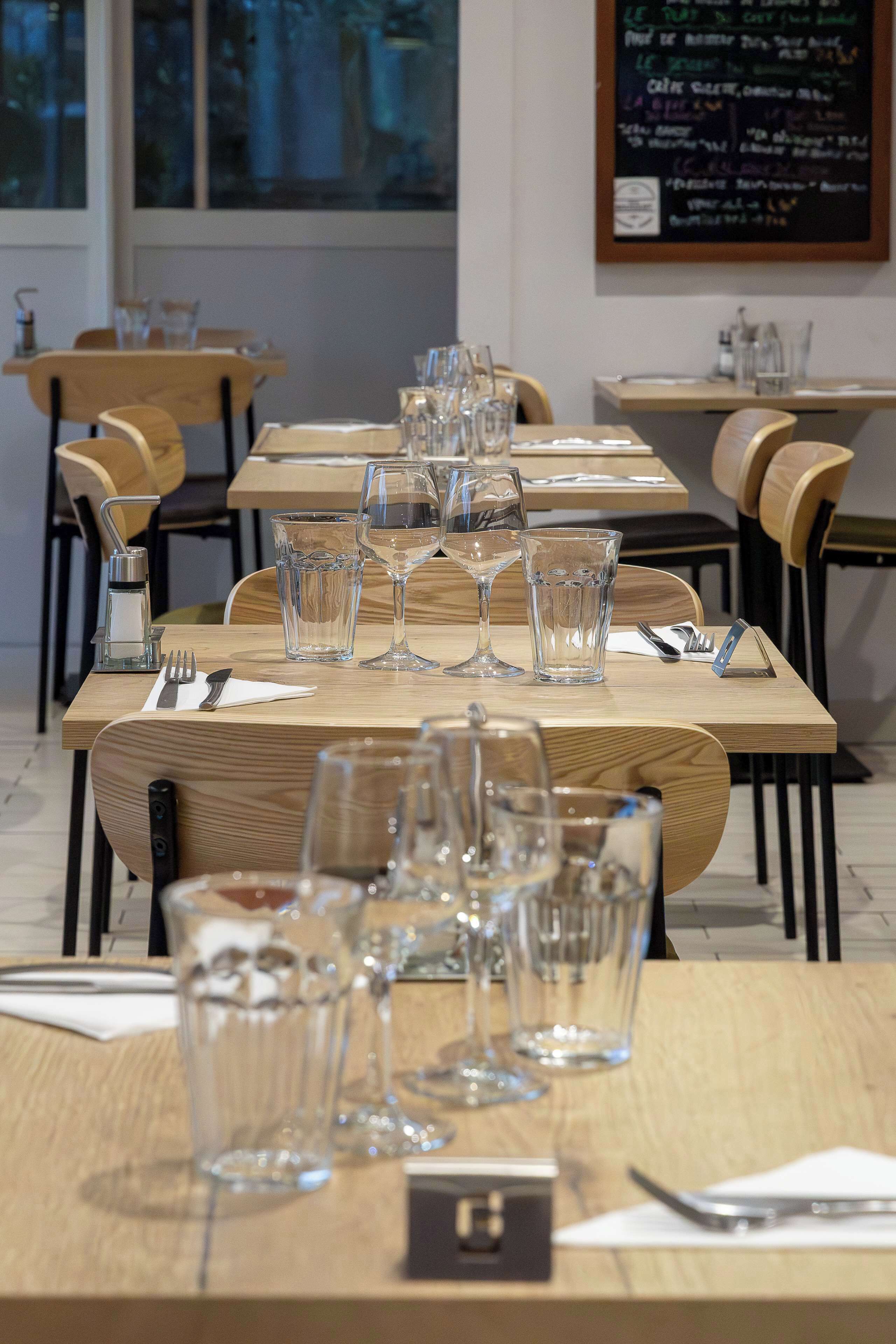 A restaurant setting with multiple tables, each set with glasses, cutlery, and napkins.