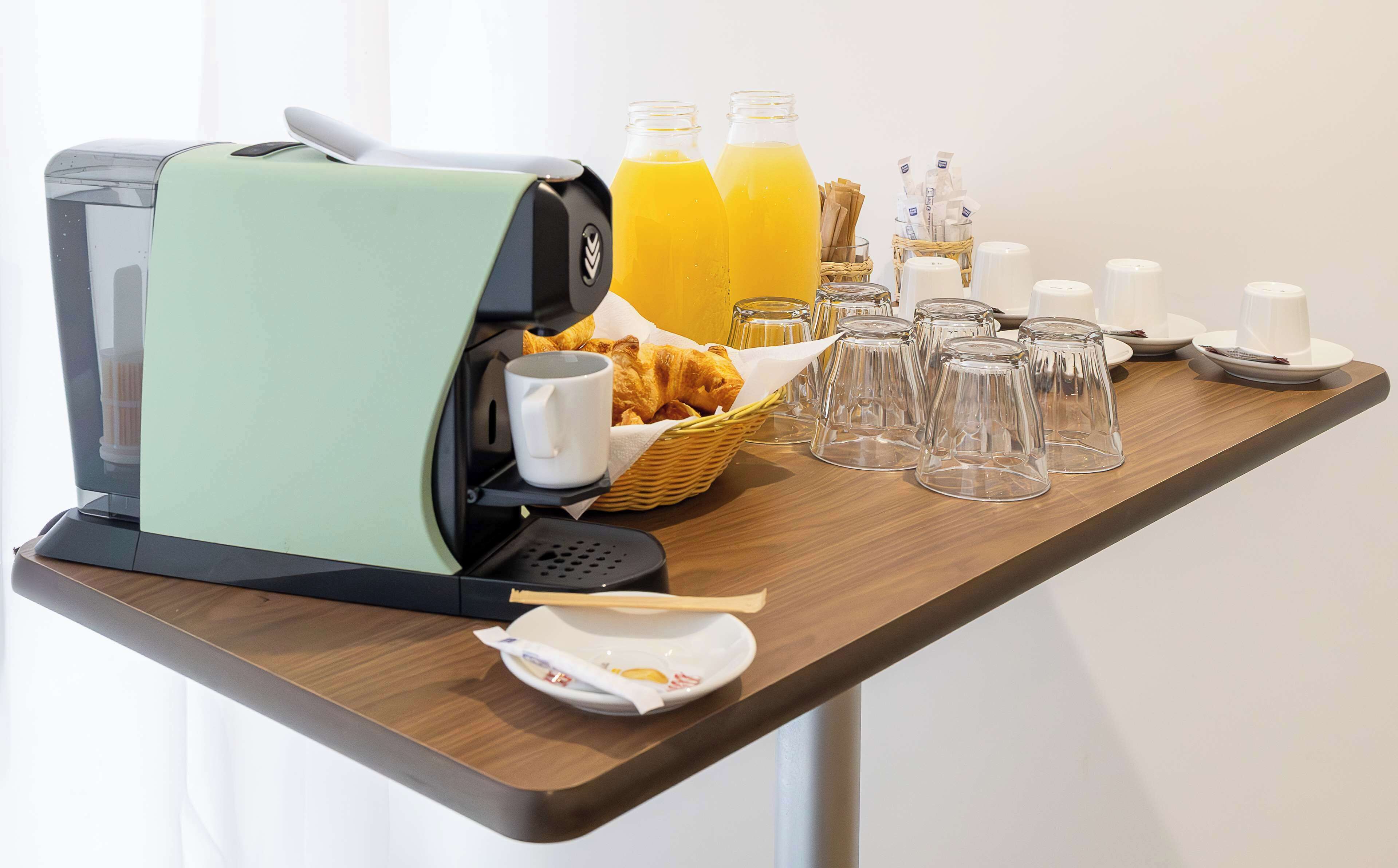 Een ontbijt met een koffiezetapparaat, croissants, sap en theeglazen op een houten tafel.