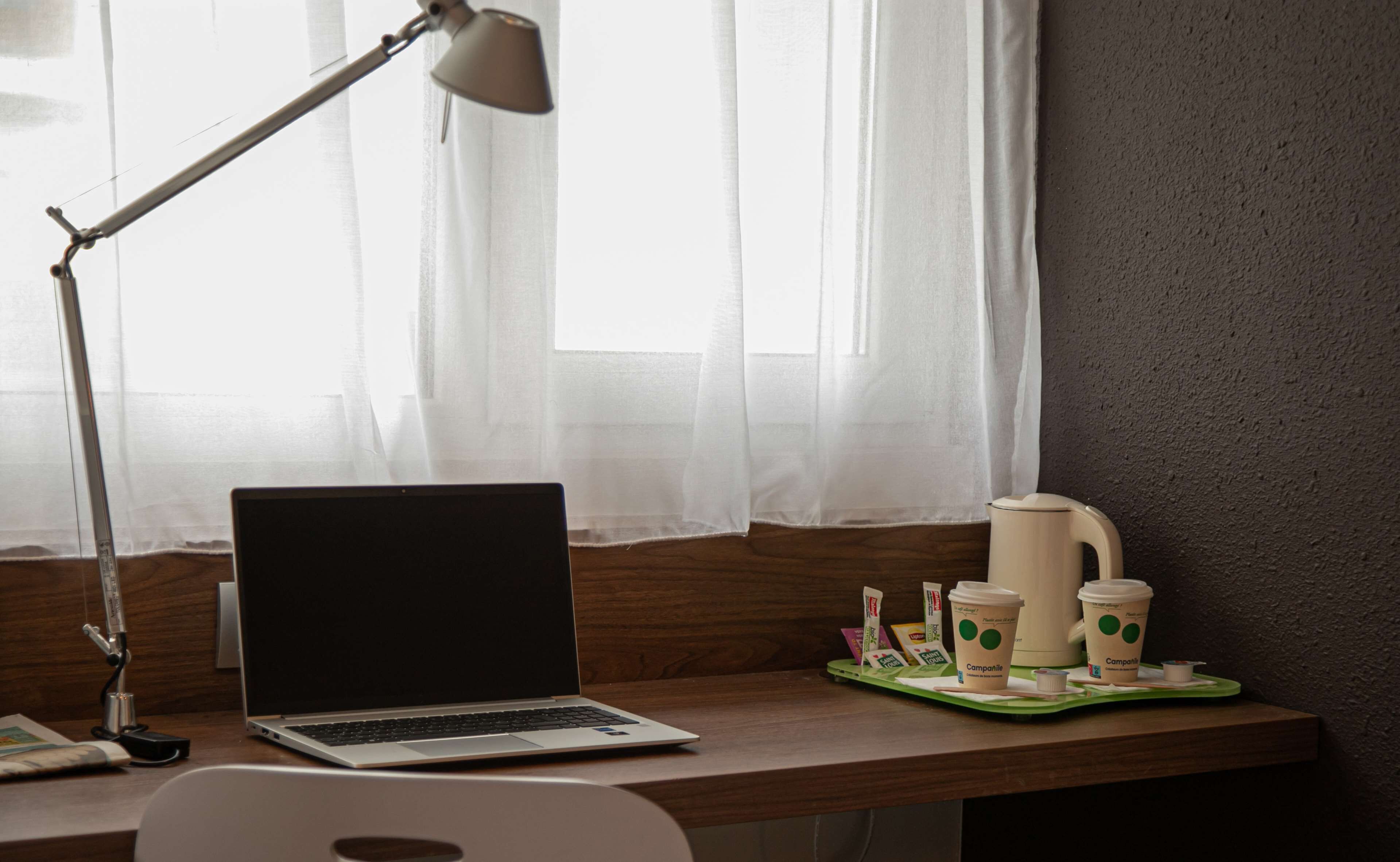 Ein Laptop auf einem Holztisch, zusammen mit einer Lampe, einer Kaffeemaschine und einer Tablett mit Kaffeetassen und einem Muffin.