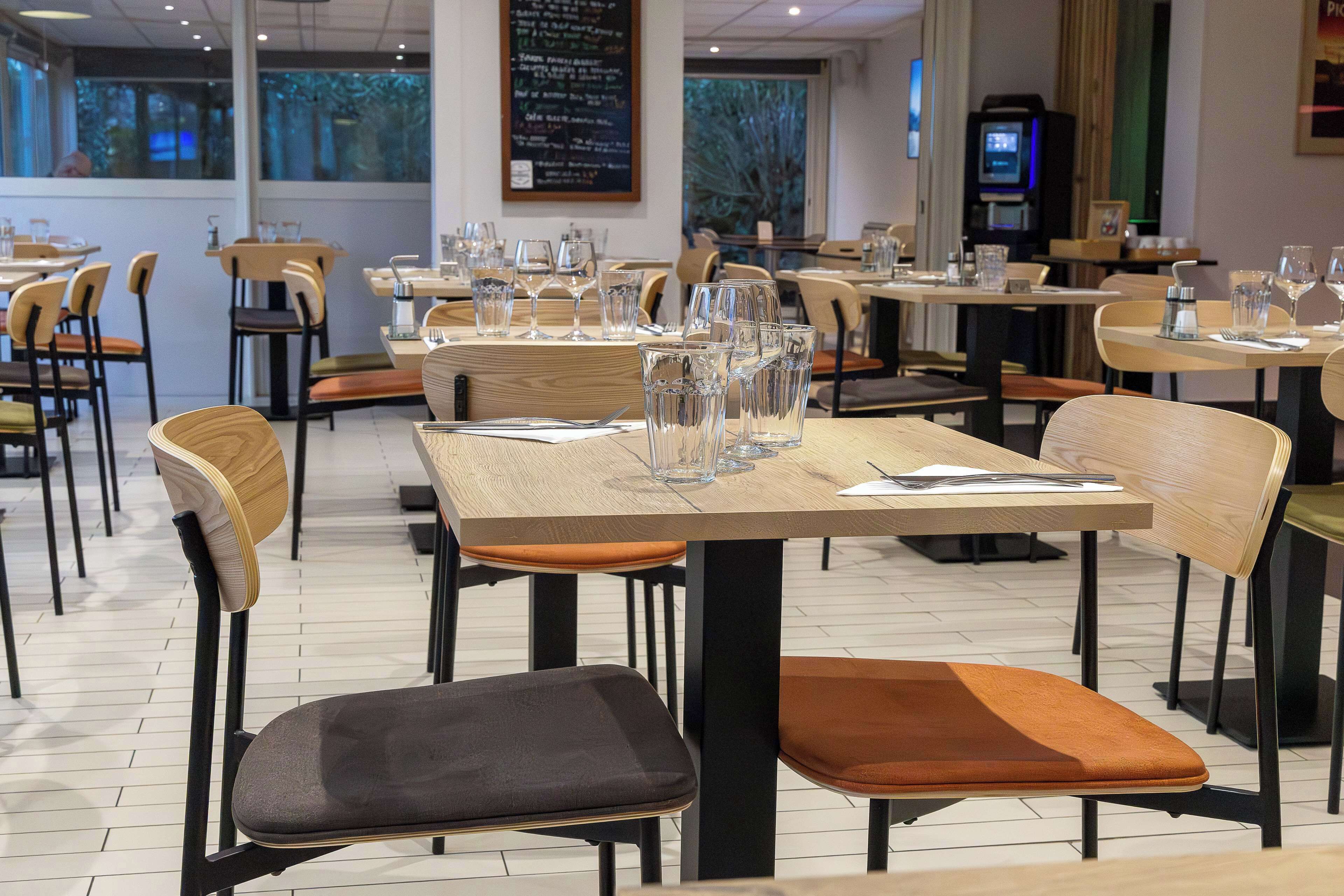 Un interno ristorante con diversi tavoli e sedie, bicchieri trasparenti e una lavagna con il menu.