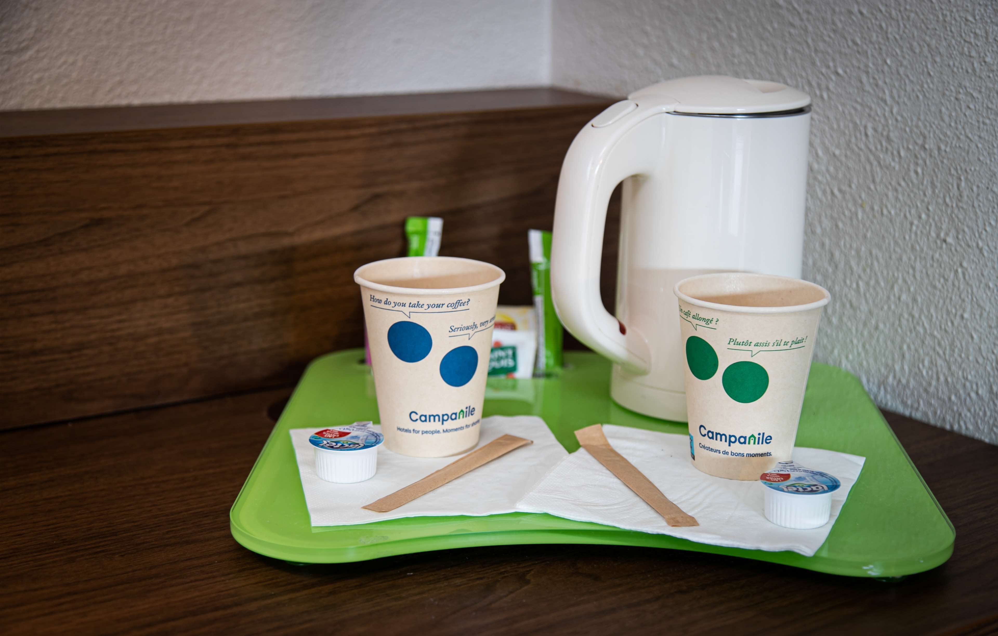 Two coffee cups with a question and answer design on a green tray, a white coffee pot, and a small container of cream.