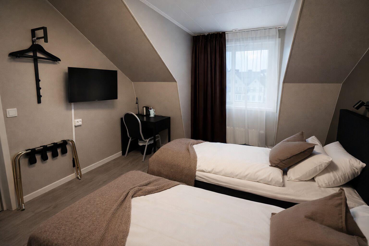 A hotel room with two beds, a desk, a chair, a TV, and a window with curtains.