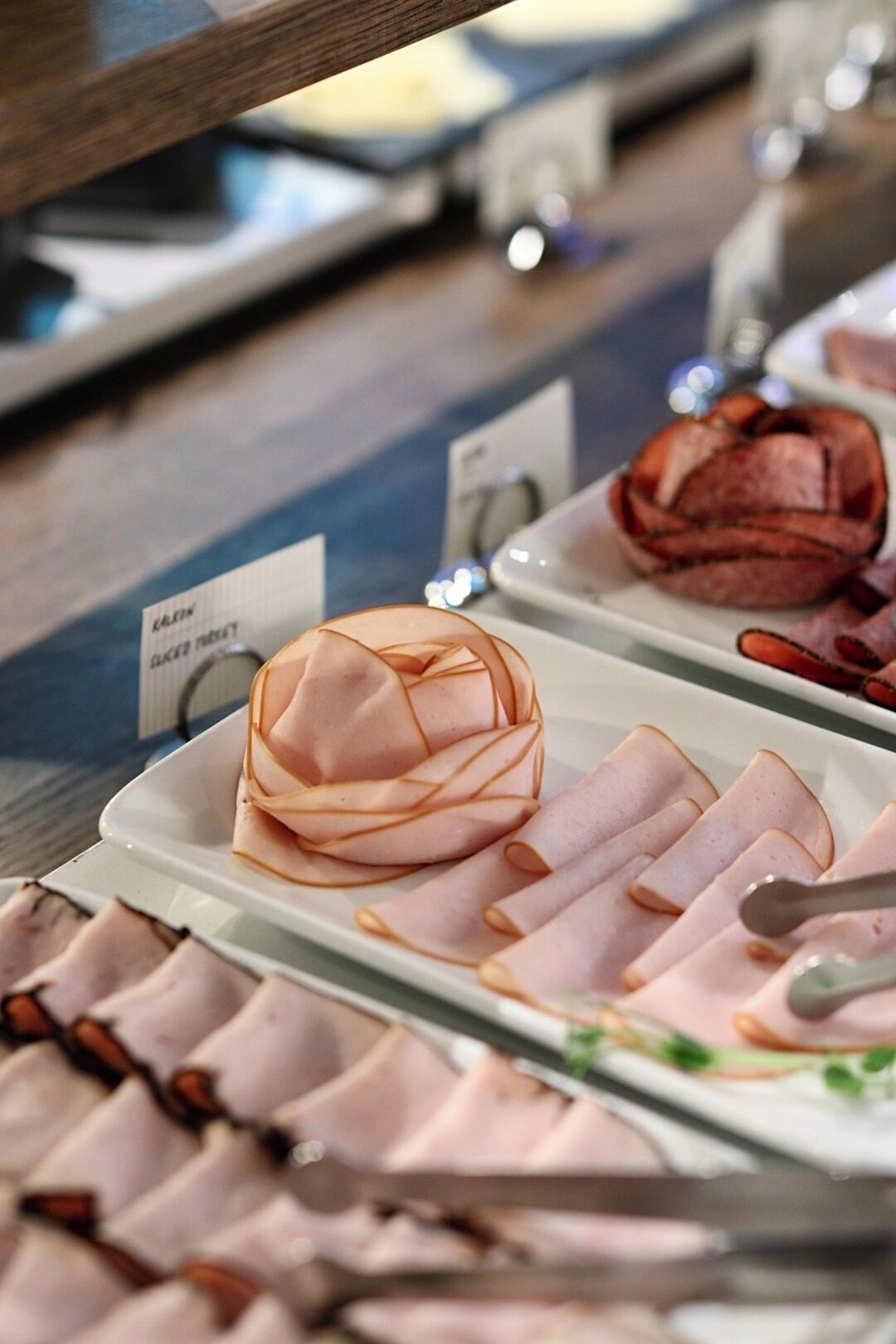 Una presentación de carnes en rodajas y un plato de carne enrollada, probablemente en una charcutería o área de servicio de alimentos.