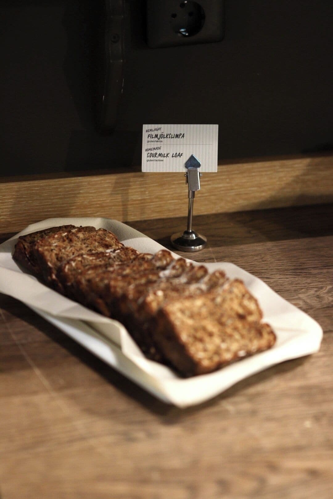 A loaf of sourdough bread on a white plate with a sign indicating it is gluten-free.