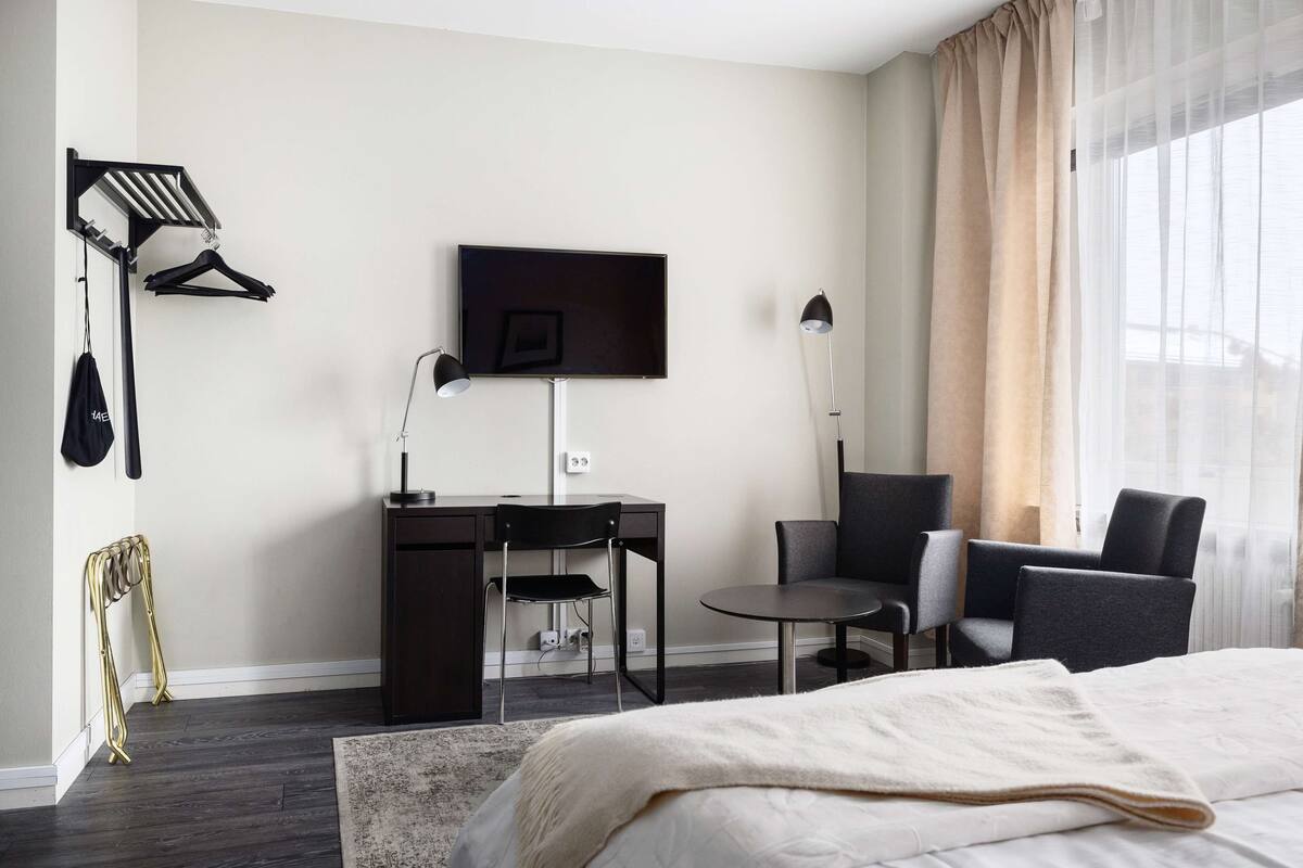 Ein modernes Hotelzimmer mit Bett, Schreibtisch, Stuhl, Fernseher und einem Fenster mit Vorhängen.