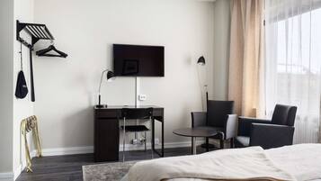 A modern hotel room with a bed, a desk, a chair, a TV, and a window with curtains.