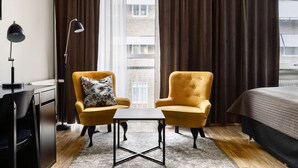 A hotel room with a bed, two yellow armchairs, a small table, a floor lamp, and a view of a building through a window with curtains. - Best Western Hotel Trollhattan (Trollhattan)