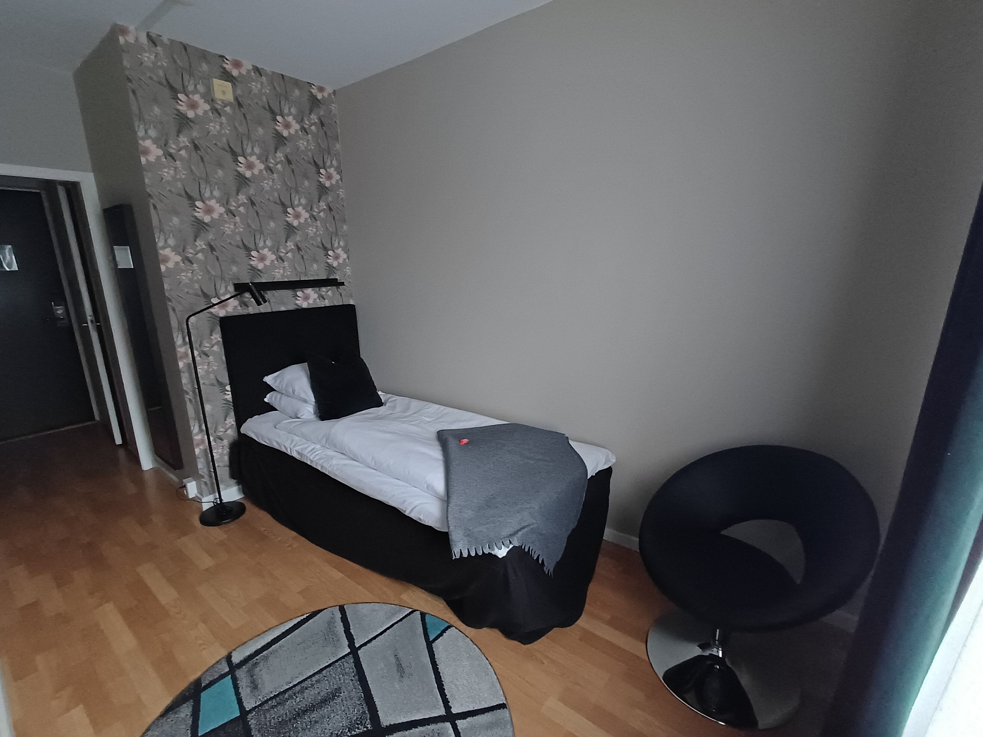Un dormitorio con una cama, un sillón negro redondo, una alfombra pequeña y una puerta.