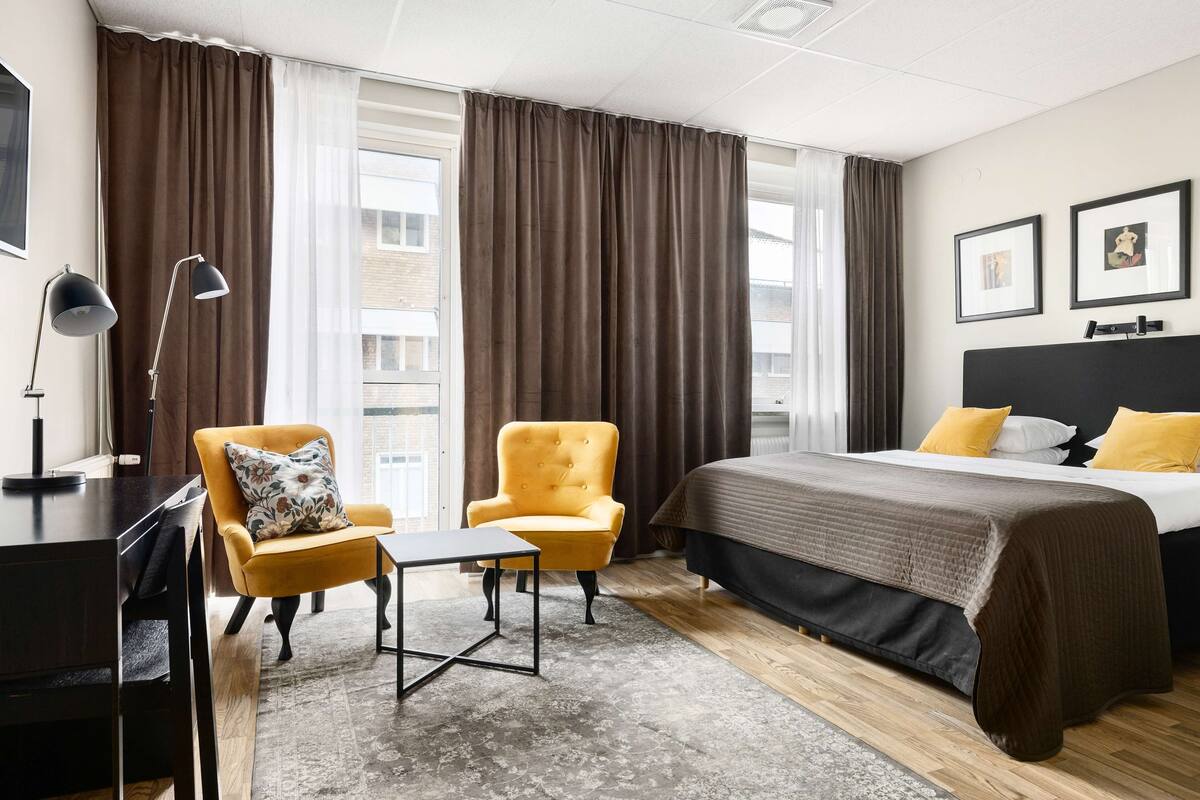 Ein Hotelzimmer mit einem Bett, zwei Sesseln, einem Schreibtisch und einer Lampe.