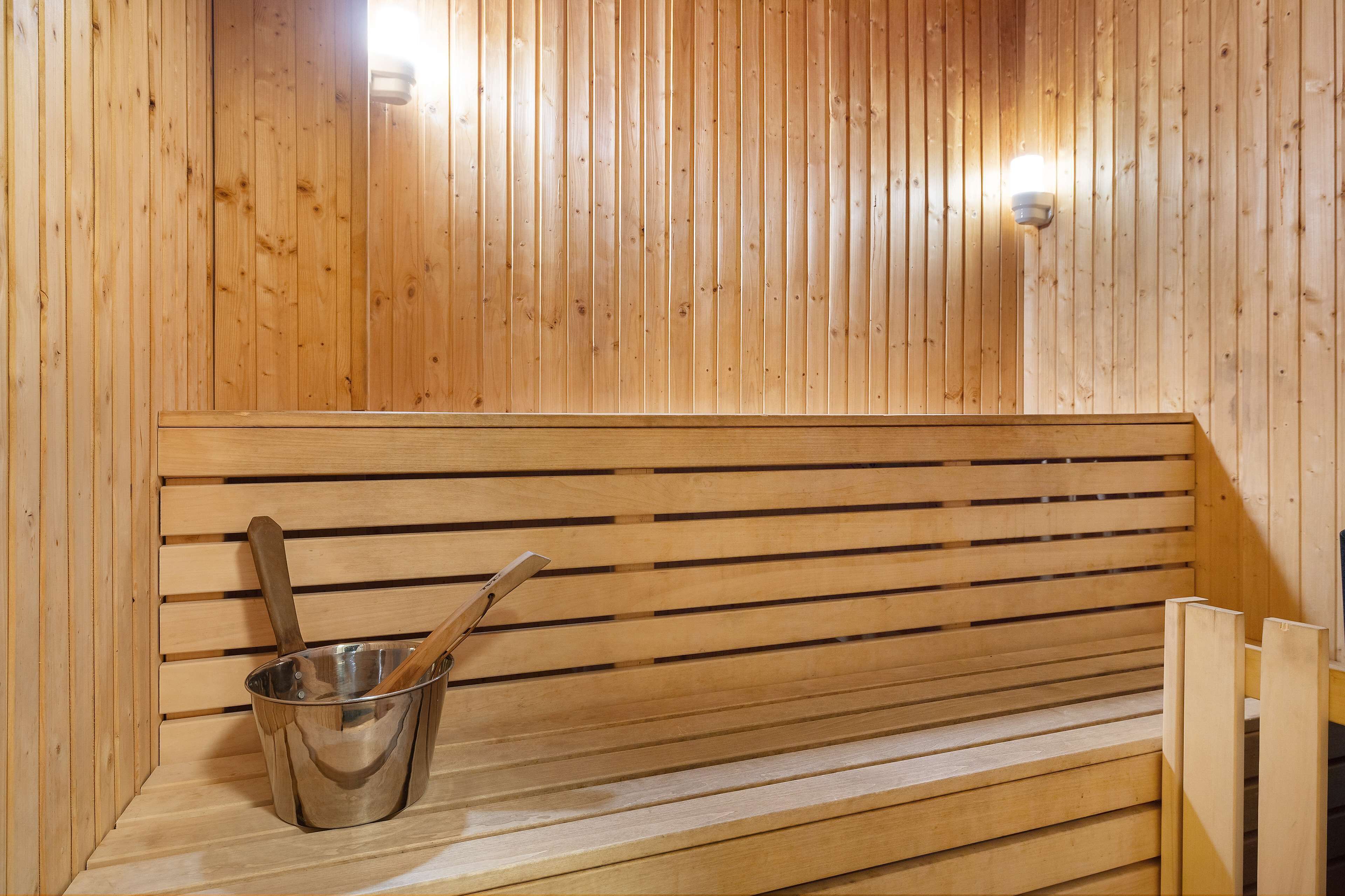 A wooden sauna bench with a metal bucket and wooden spoon.