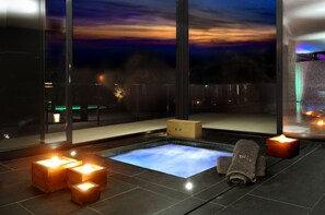 A modern spa area with a heated floor, candles, and a view of the city at dusk. - Rusticae Hotel Urbisol (Calders)