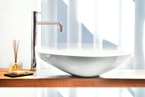 Un baño moderno con un lavamanos blanco de diseño, un grifo cromado y una encimera de madera.