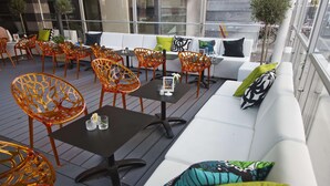 An outdoor seating area with wicker chairs, a black table, and a white sofa with colorful cushions. - Scandic Karlstad City (Karlstad)