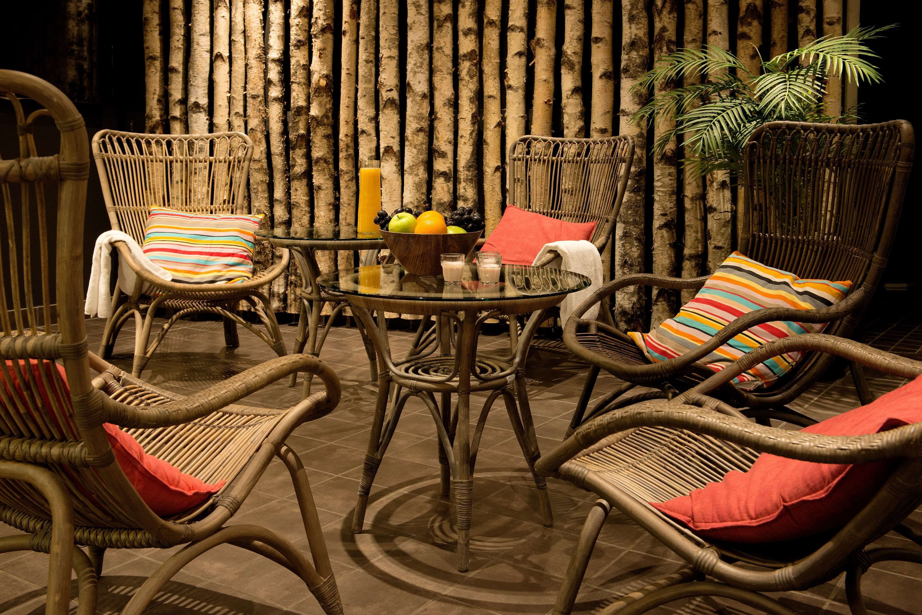 Wicker stoelen met kleurrijke kussens rondom een glazen tafel met fruit en drankjes.