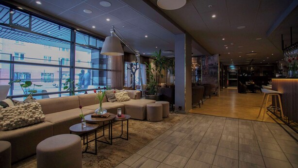 A modern hotel lobby with a large sofa, round tables, and a bar area. - Scandic Karlstad City (Karlstad)