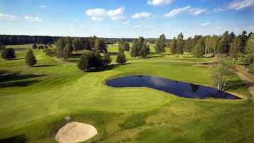 Un campo de golf con un estanque, árboles y cielo despejado.