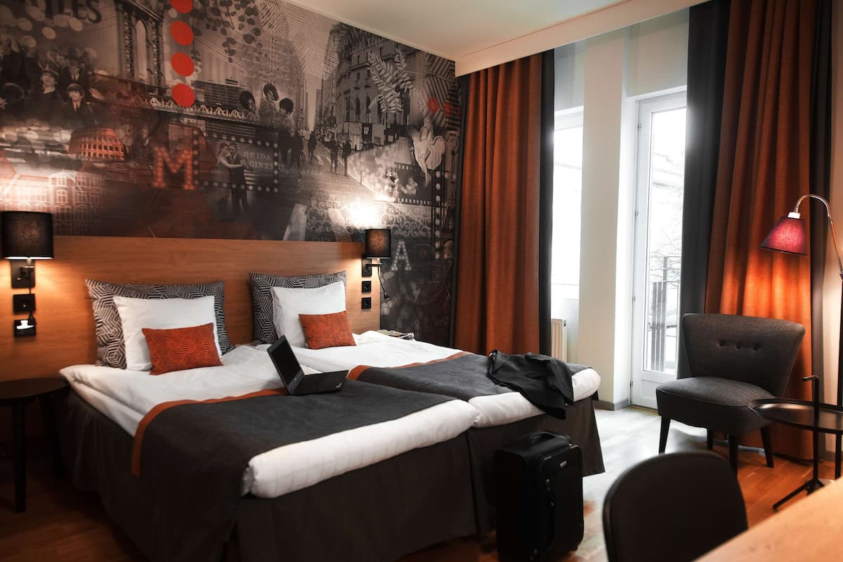 Ein Hotelzimmer mit einem großen Bett, einem Schreibtisch, einem Stuhl, einem Laptop und einem Koffer.