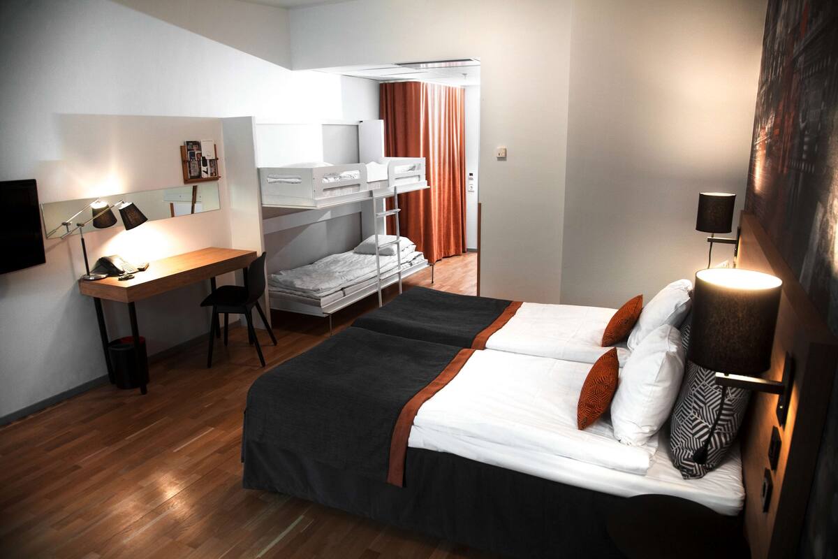 Ein Hotelzimmer mit einem Etagenbett, einem Schreibtisch mit Stuhl, einer Schreibtischlampe und einem Nachttisch mit Lampe.