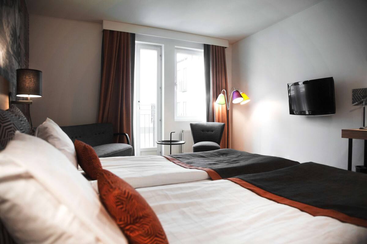 Ein Hotelzimmer mit zwei Betten, einem Sofa, einem Fernseher und Blick ins Freie.