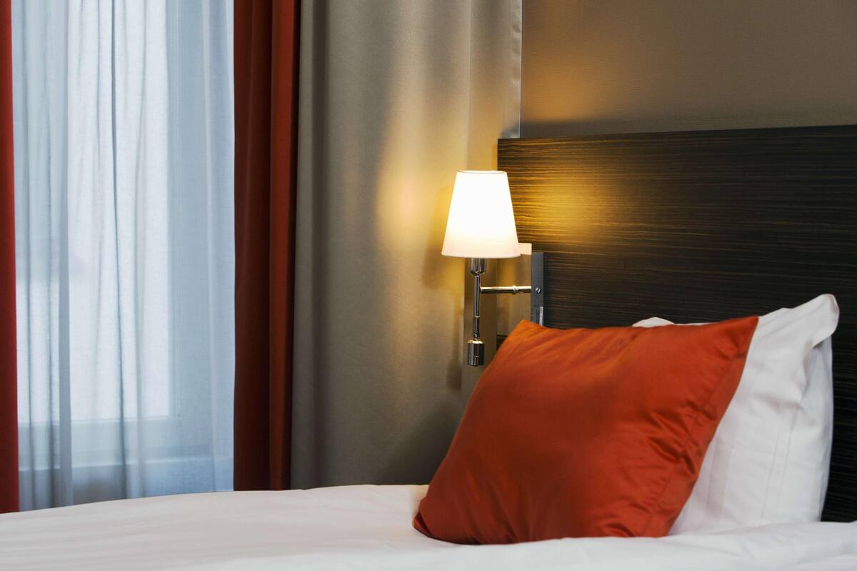 A hotel room with a bed, a lamp, and curtains.