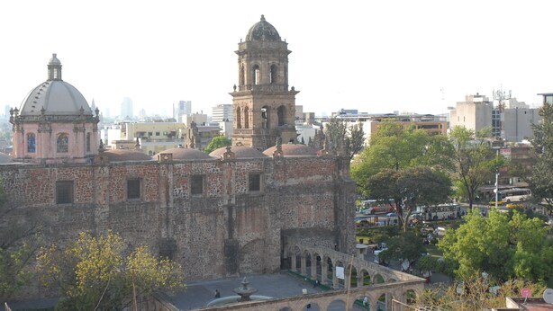 Un edificio histórico con una cúpula y un campanario, rodeado de árboles y un patio.