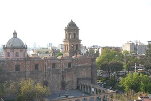 Un edificio histórico con una cúpula y un campanario, rodeado de árboles y un patio.