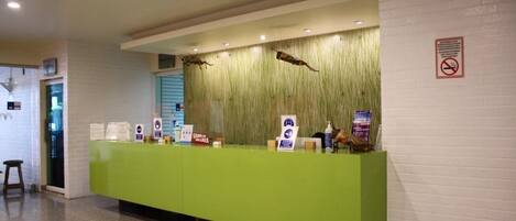 A reception desk with a green counter, informational signs, and a wall-mounted decorative element.