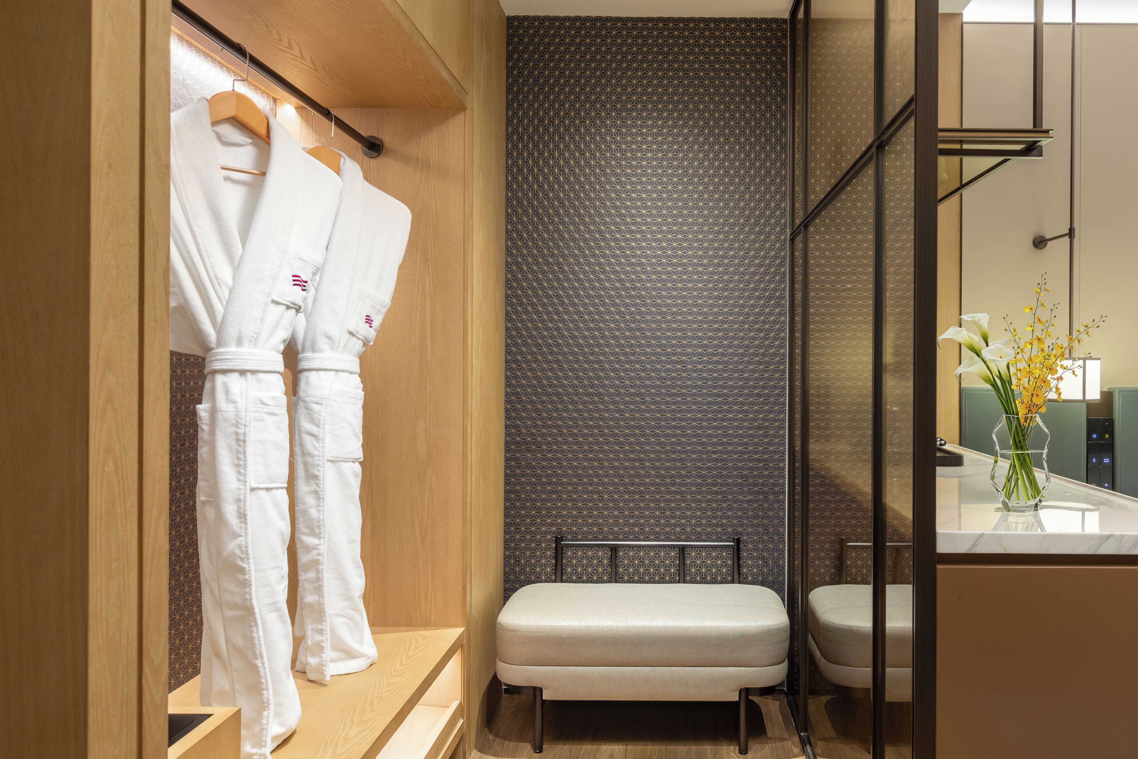 A modern bathroom with a wooden vanity, a bench, and a patterned wall.